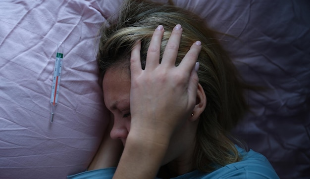 Photo jeune femme au lit et tenant sa tête près du thermomètre à mercure