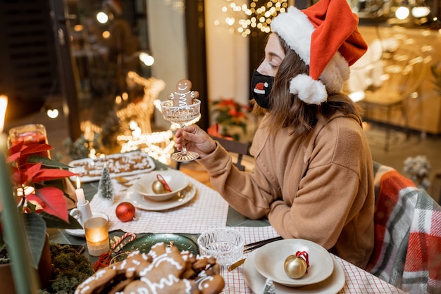 Jeune femme au masque facial célébrant seule les vacances du Nouvel An à la maison. Concept de quarantaine et d'auto-isolement pendant l'épidémie en vacances