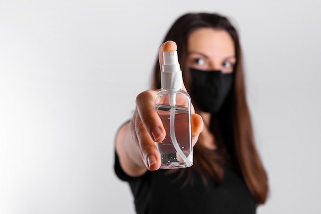 Jeune femme au masque noir tient un gel d'alcool pour désinfecter les mains. Pandémie de covid-19