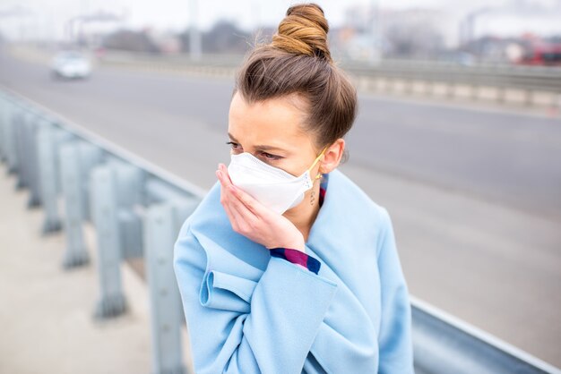 Jeune femme au masque de protection se sentant mal dans la rue de la ville avec la pollution de l'air