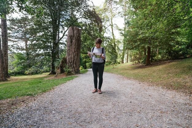 Jeune femme au milieu d'une forêt regardant une carte dans une forêt suivant un itinéraire