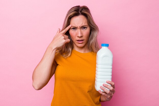 Jeune femme australienne tenant une bouteille de lait isolée sur fond rose montrant un geste de déception avec l'index.