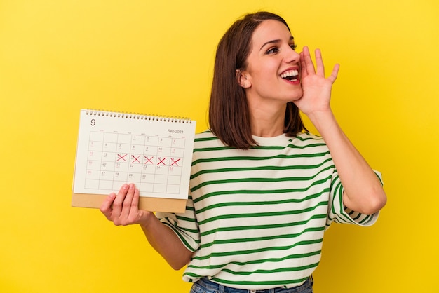 Jeune femme australienne tenant un calendrier isolé sur fond jaune criant et tenant la paume près de la bouche ouverte.