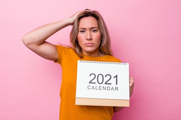 Jeune femme australienne tenant un calendrier isolé sur fond rose étant choquée, elle s'est souvenue d'une réunion importante.