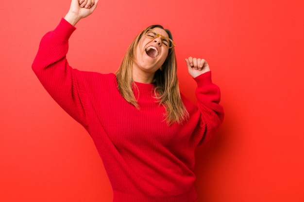 Jeune femme authentique, de vraies personnes charismatiques, contre un mur, célébrant une journée spéciale, saute et lève les bras avec énergie.