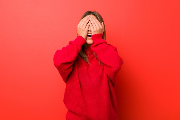 Jeune femme authentique, de vraies personnes charismatiques, contre un mur, couvre les yeux avec les mains, un large sourire attendait une surprise.