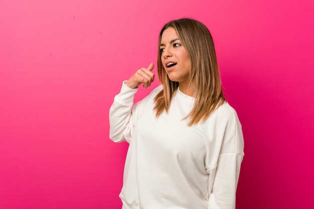 Jeune femme authentique de vraies personnes charismatiques contre un mur, montrant un geste d'appel avec les doigts.