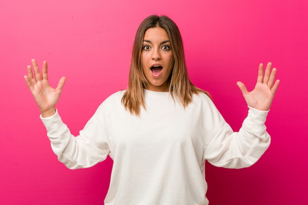 Jeune femme authentique, de vraies personnes charismatiques, contre un mur, recevant une agréable surprise, excitée et levant les mains.