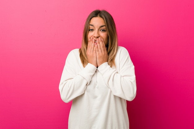 Jeune femme authentique de vrais gens charismatiques contre un mur en riant de quelque chose, couvrant la bouche avec les mains.