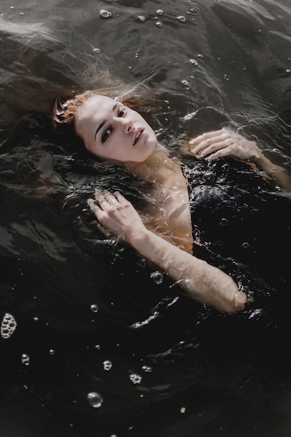 Jeune femme aux bras levés dans l'eau. Eau noire. Photo verticale