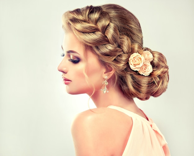 Photo jeune femme aux cheveux blonds avec un mariage élégant à la mode ou une coiffure de soirée avec une large tresse entourant sa tête et un maquillage vif sur son visage