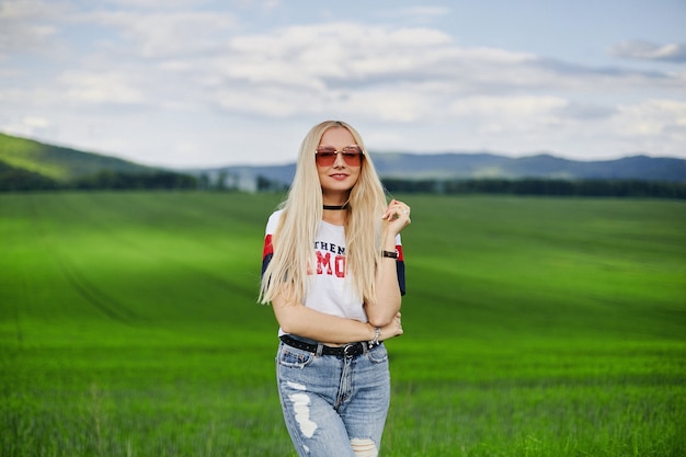 Jeune femme aux cheveux blonds portant des jeans et un t-shirt posant dans la campagne