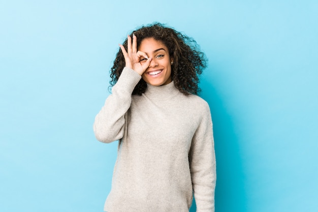 Jeune femme aux cheveux bouclés afro-américaine excité en gardant le geste ok sur les yeux.