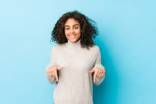 Jeune femme aux cheveux bouclés afro-américaine pointe vers le bas avec les doigts, sentiment positif.