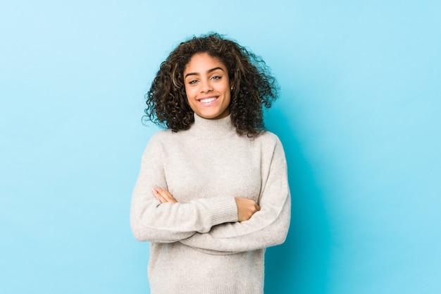 Jeune femme aux cheveux bouclés afro-américaine qui se sent confiante, croisant les bras avec détermination.