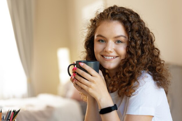 Jeune femme aux cheveux bouclés se détendre à l'intérieur à la maison avec une tasse de café