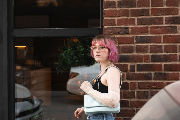 Photo jeune femme aux cheveux de couleur rose debout devant le mur de briques en plein air et regardant la caméra