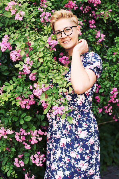 Jeune femme aux cheveux courts près d'un buisson de fleurs