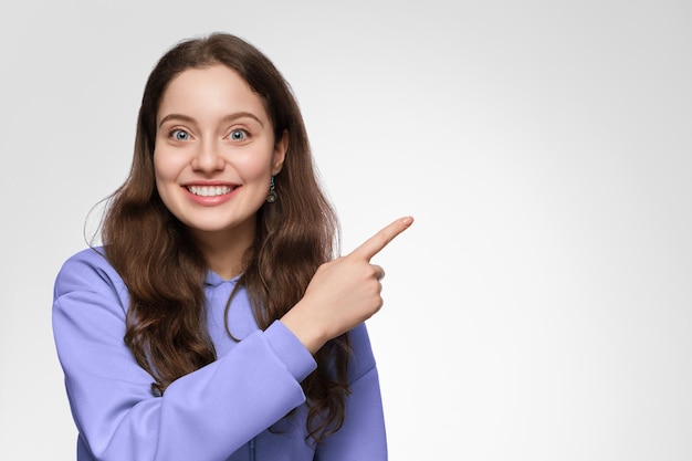 Une jeune femme aux cheveux longs et aux yeux bleus pointe son doigt vers le côté droit. La fille porte un sweat à capuche violet surdimensionné