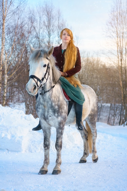 Jeune femme aux cheveux longs à cheval en hiver