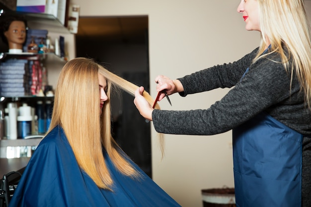 Jeune femme aux cheveux longs chez le coiffeur. Styliste faisant la coiffure avec des ciseaux et un peigne.