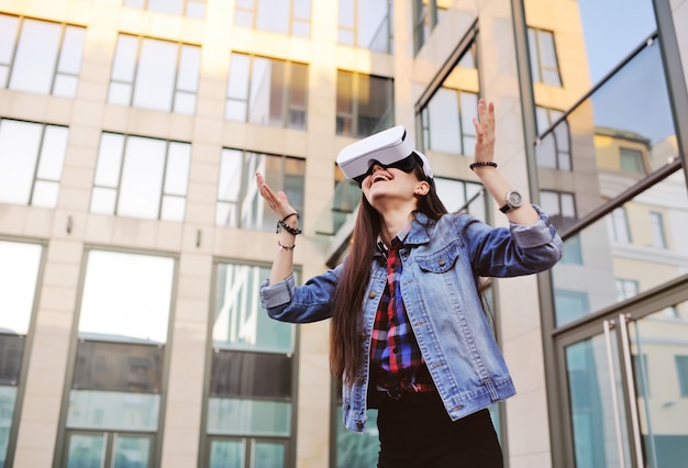 Jeune femme aux cheveux longs dans des lunettes de réalité virtuelle sur un bâtiment de verre moderne