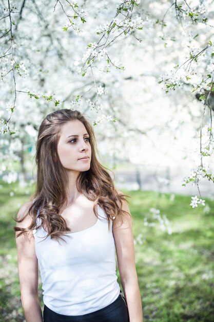 Jeune femme aux cheveux longs dans un tshirt blanc sous les arbres en fleurs