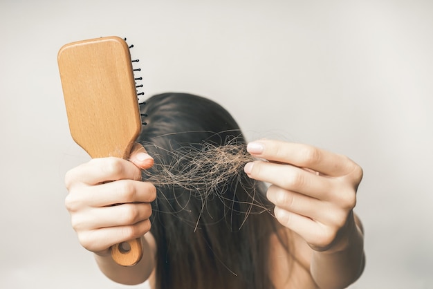 Une jeune femme aux cheveux longs est agacée par la perte de cheveux, tient un peigne et ses cheveux à la main, cache ses yeux