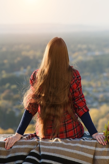 Jeune femme aux cheveux longs est assise sur une colline surplombant le village. Vue arrière