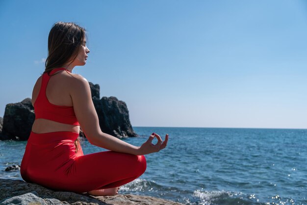 Jeune femme aux cheveux longs instructeur de fitness en Sportswear Leggings et Tops s'étirant avant le pilates sur un tapis de yoga près de la mer lors d'une journée ensoleillée concept de routine de yoga fitness féminin