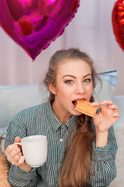 Jeune femme aux cheveux longs prend son petit déjeuner au lit des gaufres le jour de la Saint-Valentin