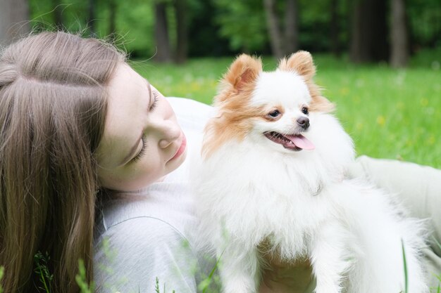 Une jeune femme aux cheveux longs se trouve sur la pelouse du parc avec un chien de Poméranie