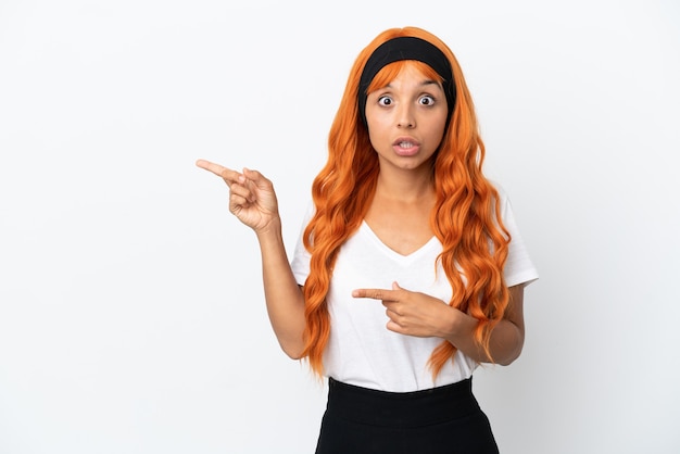 Photo jeune femme aux cheveux orange isolé sur fond blanc surpris et pointant du côté