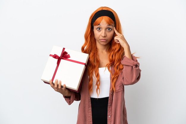 Jeune femme aux cheveux orange tenant un cadeau isolé sur fond blanc en pensant à une idée