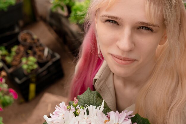 Jeune femme aux cheveux roses et blonds tenant des fleurs roses dans le jardin