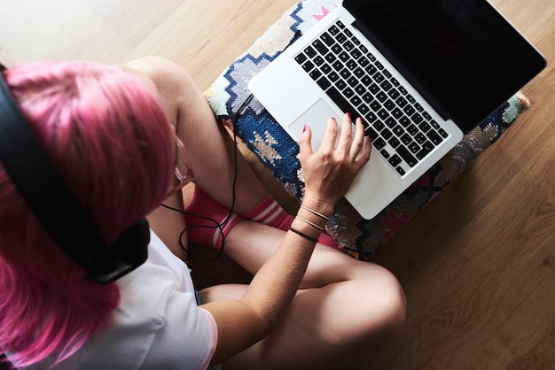 Jeune femme aux cheveux roses portant des écouteurs et utilisant un ordinateur portable à la maison