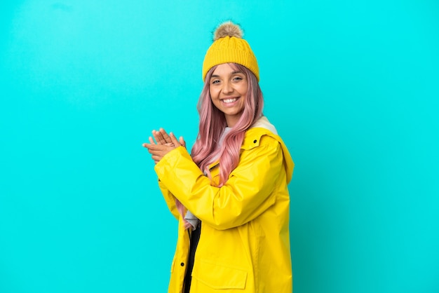 Jeune femme aux cheveux roses portant un manteau imperméable isolé sur fond bleu applaudissant