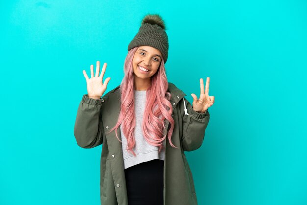 Jeune femme aux cheveux roses portant un manteau imperméable isolé sur fond bleu comptant huit avec les doigts