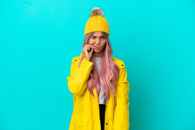 Jeune femme aux cheveux roses portant un manteau imperméable isolé sur fond bleu montrant un geste de silence