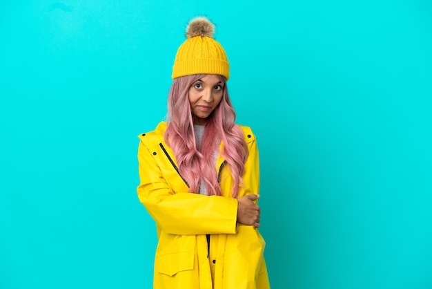 Jeune femme aux cheveux roses portant un manteau imperméable isolé sur fond bleu en riant