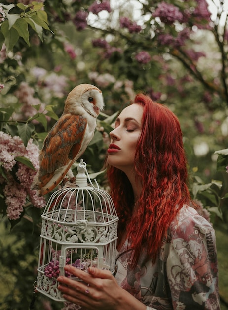 Jeune femme aux cheveux rouges dans un jardin de lilas avec une chouette effraie des clochers