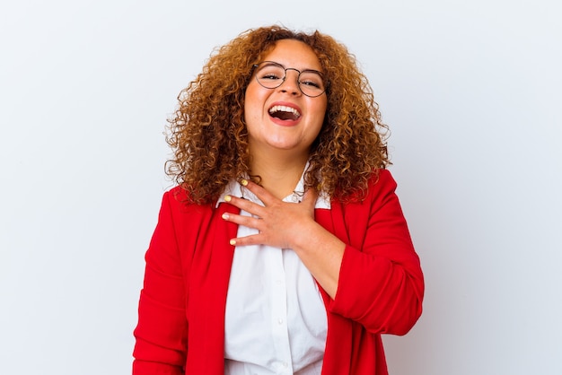 Jeune femme aux courbes latines isolées sur fond blanc éclate de rire en gardant la main sur la poitrine.