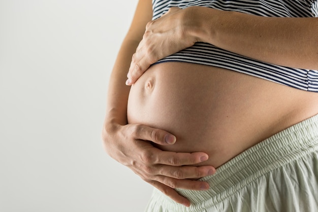 Jeune femme aux derniers stades de la grossesse berçant son ventre nu avec ses mains alors qu'elle partage un moment de tendresse avec son enfant à naître.