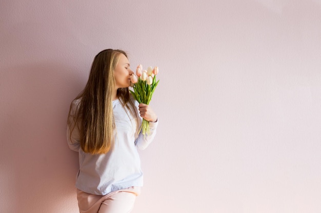 Jeune femme aux longs cheveux blonds lâches garde les fleurs de printemps entre les mains d'une journée ensoleillée