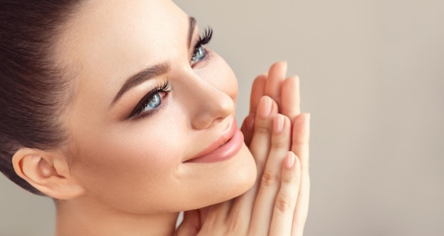 Une jeune femme aux yeux bleus avec un doux maquillage sur le visage touche le visage Traitement du visage et beauté