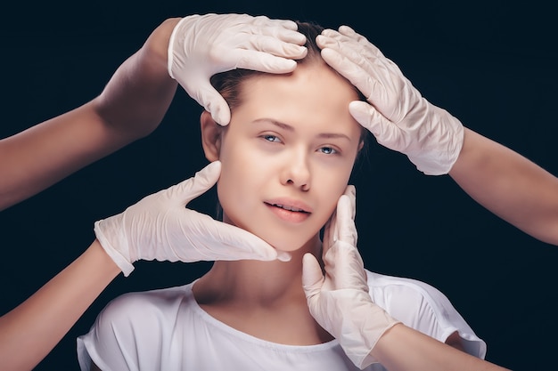 Jeune femme aux yeux fermés ayant un examen médical de la peau de son visage par des médecins en plastique