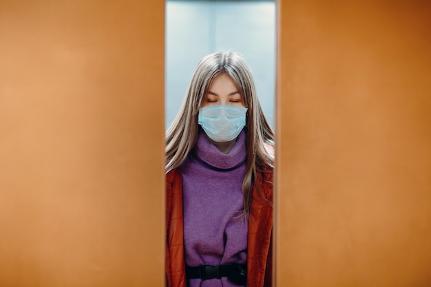 Jeune femme aux yeux fermés, debout dans l'ascenseur en masque médical. Les portes se ferment. Concept de pandémie de coronavirus COVID-19.