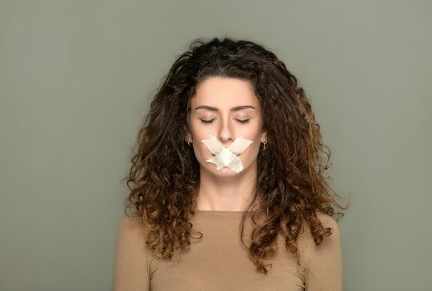 Jeune femme aux yeux fermés et sa bouche fermée dans un concept de censure de la vision et de la liberté d'expression sur un fond gris studio