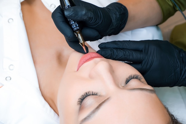 Jeune femme ayant un maquillage permanent sur les lèvres au salon des esthéticiennes. Fond vert naturel