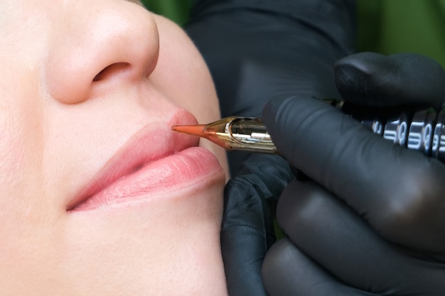 Jeune femme ayant un maquillage permanent sur les lèvres au salon des esthéticiennes. Fond vert naturel